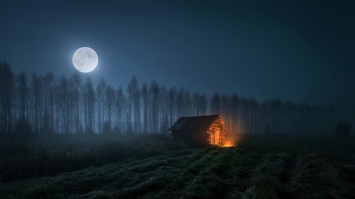 Cabin in a field at night with a full moon