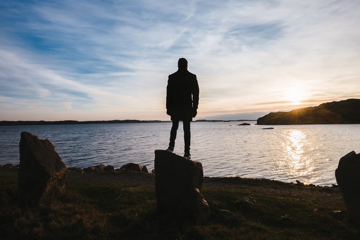 Silhouette of a person standing on a rock by the sea at sunset