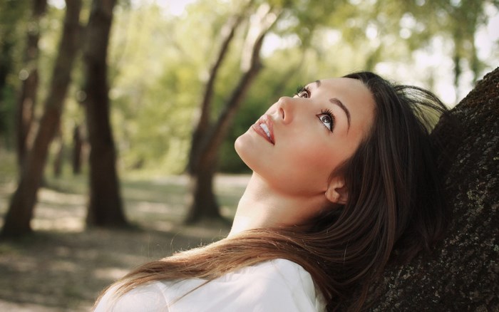 Young woman leaning against a tree outdoors