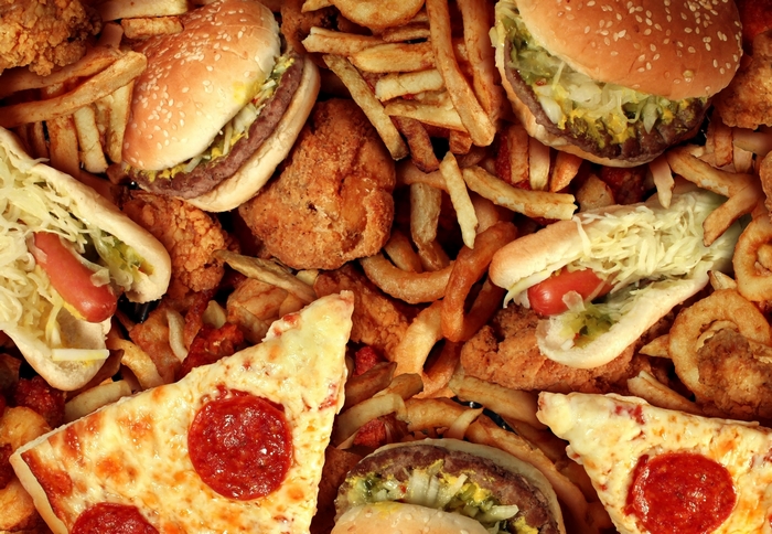 A pile of fast food including burgers, fries, pizza, and hot dogs