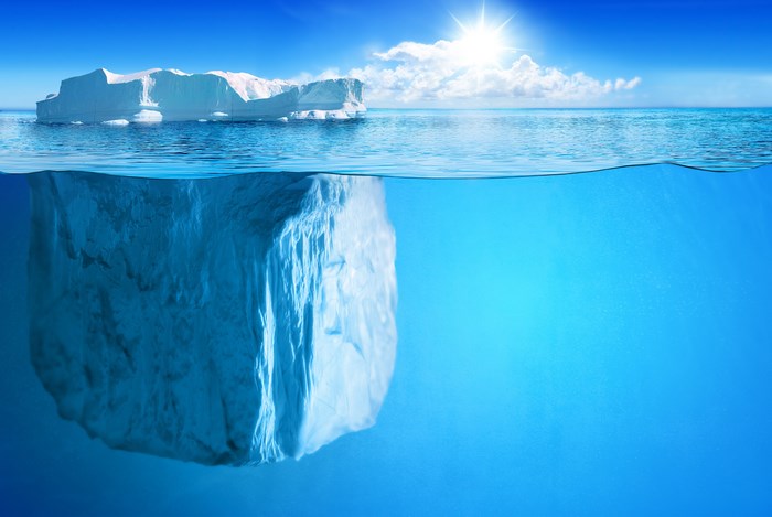 Iceberg floating in the ocean with sun and clouds