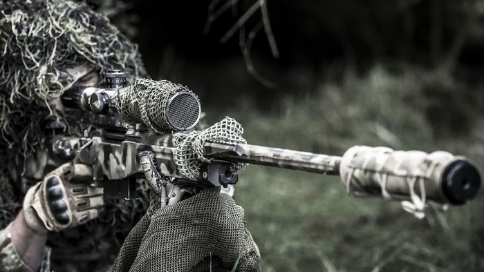 Sniper in ghillie suit aiming rifle