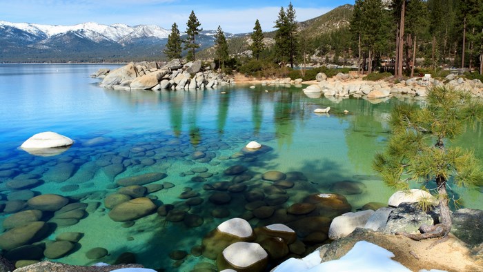 Crystal clear lake with snow-capped mountains and pine trees