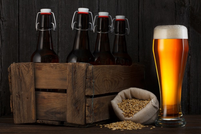 Beer bottles in a crate with a glass of beer and barley