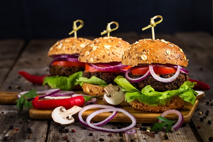 Three vegan burgers with red onion and lettuce