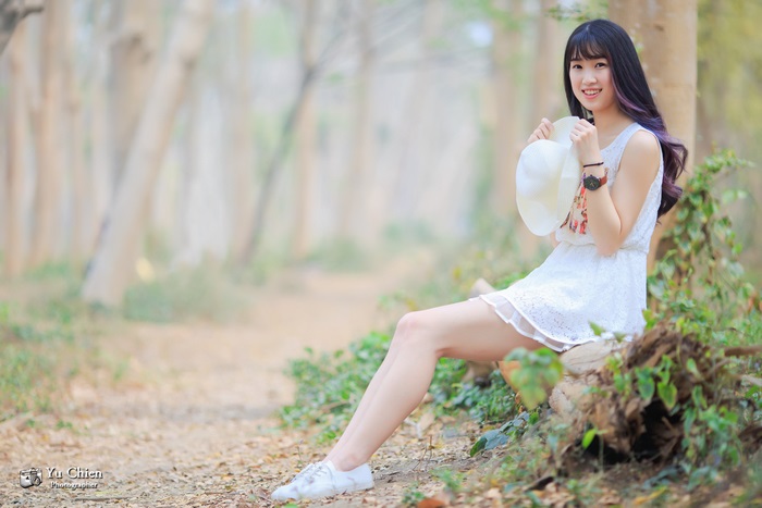 Asian woman in white dress holding hat in forest