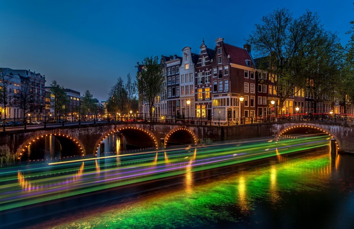 Amsterdam canal bridge at dusk with boat light trails