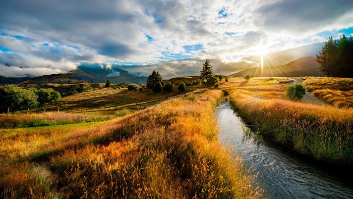 Sunset over a river in a grassy field with mountains