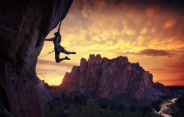 Rock climber suspended on cliff face at sunset
