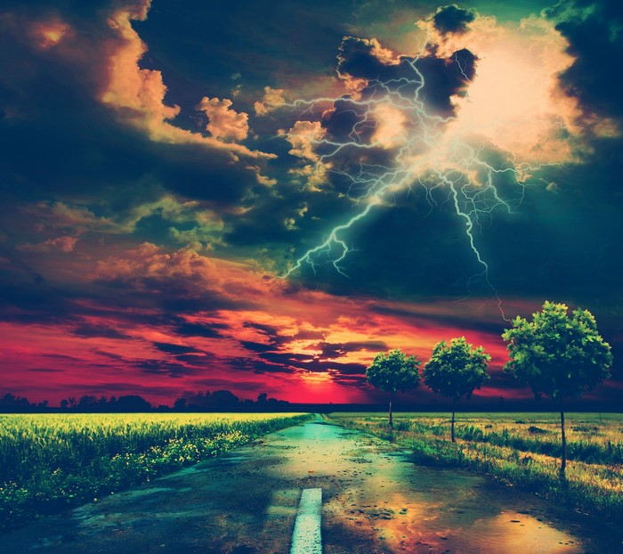 Road through a field during a lightning storm