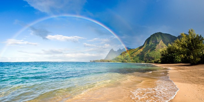 Rainbow over beach with mountains and ocean