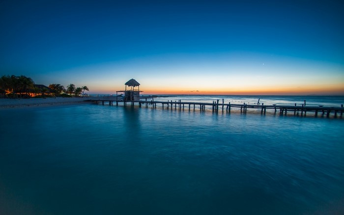 Tropical beach pier at sunset with ocean and palm trees