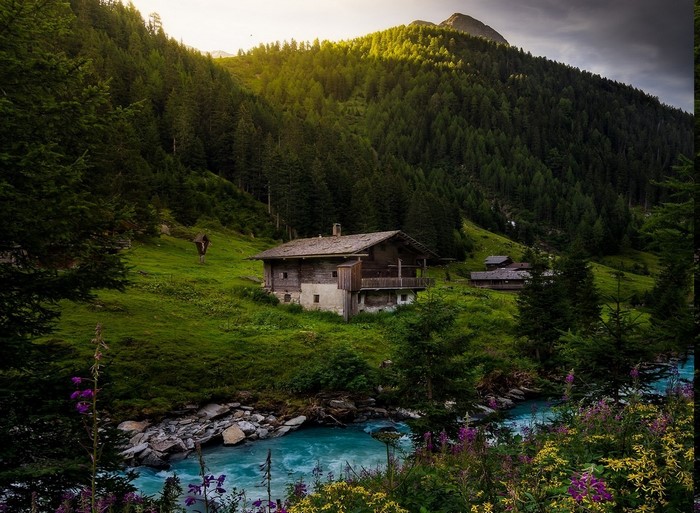 Alpine cottage by a turquoise river with a forest backdrop