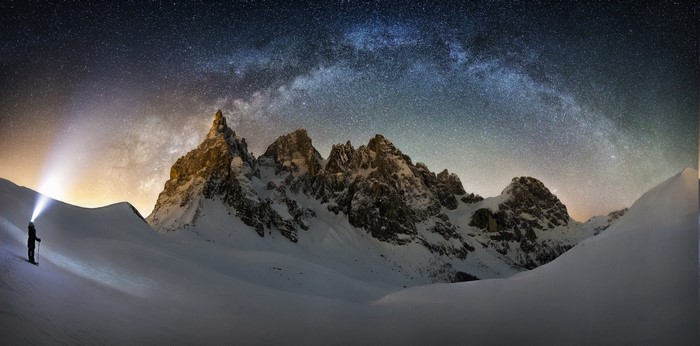 Snowy mountains under the Milky Way with a person with a headlamp