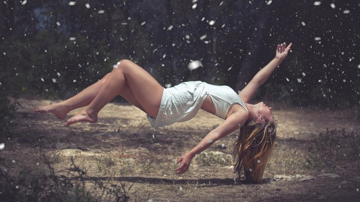 Woman in white dress floating in forest with snowflakes