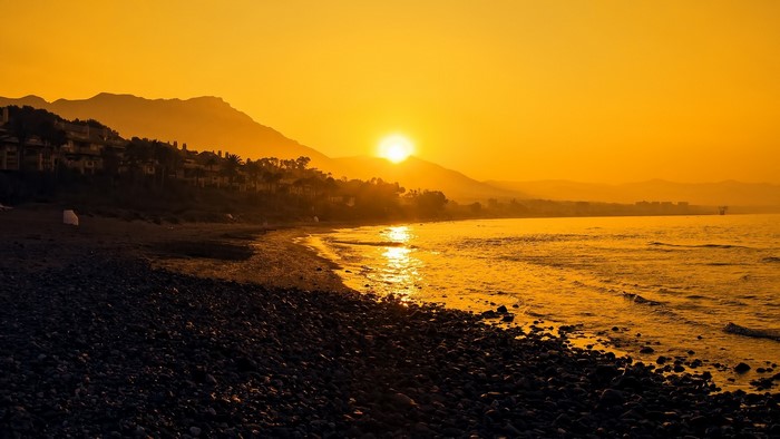 Sunset over a pebble beach with mountains and buildings