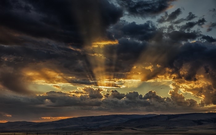 Sun rays breaking through dark clouds over hills
