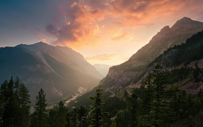 Mountain valley at sunset with clouds and trees