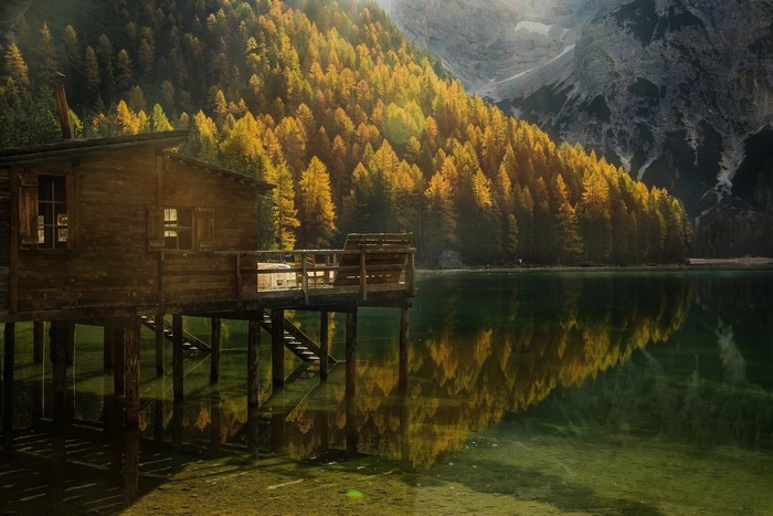 Wooden cabin on stilts by a lake with autumn forest and mountains