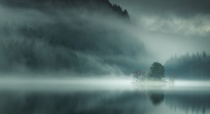 Misty lake with island and forest in Scotland
