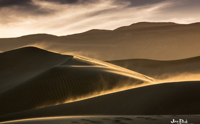 Sand dunes with wind blowing sand at sunset