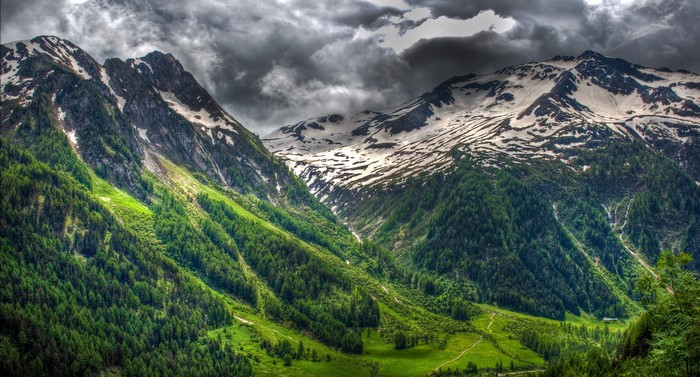 Green mountain valley with snowy peaks and stormy clouds