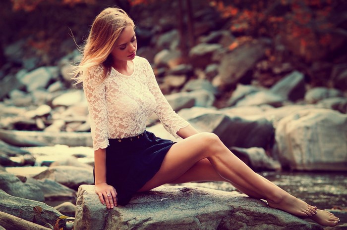 Woman with blonde hair sitting on rocks by water