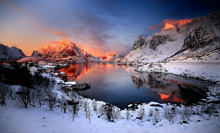 Snowy mountains and village by the water at sunset