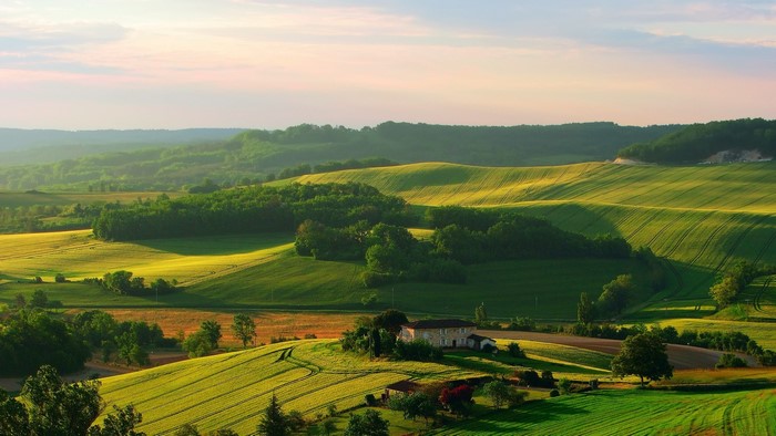 Rolling green hills with a house at sunset