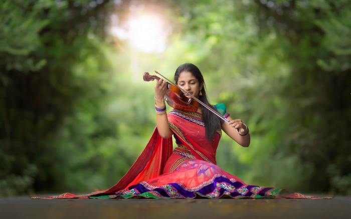Woman playing violin in a red saree outdoors