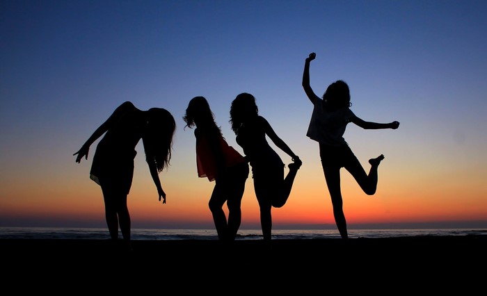 Silhouettes of four women dancing on a beach at sunset