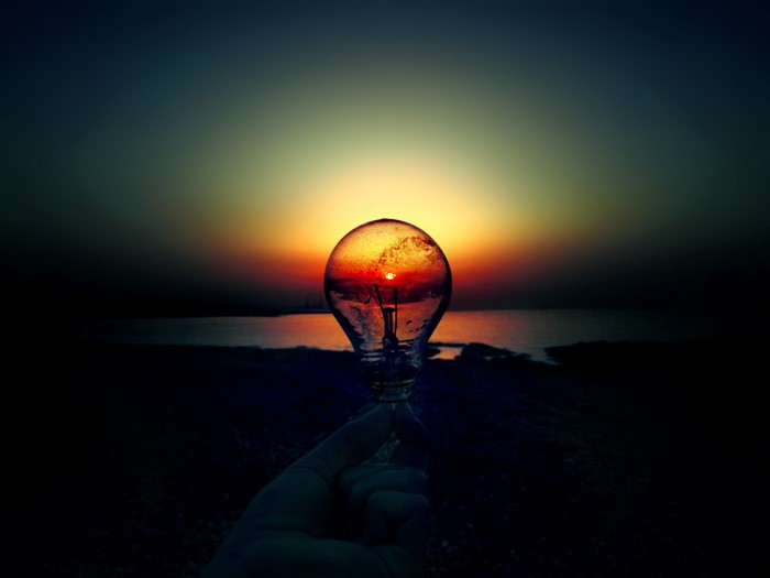 Light bulb with sunset reflection held by hand