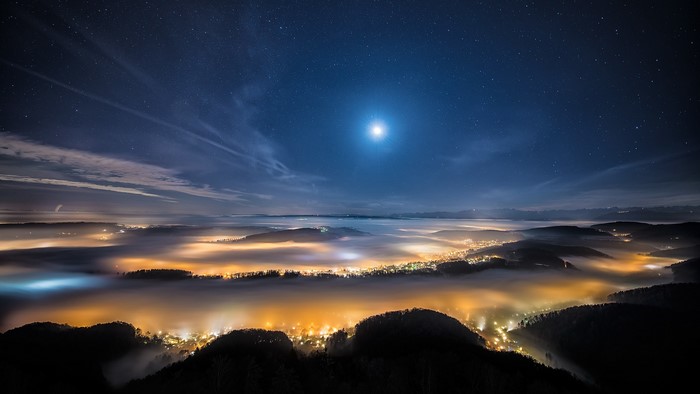 Night sky over a misty valley with city lights