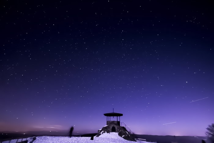 Starry night sky over a snowy landscape with a gazebo