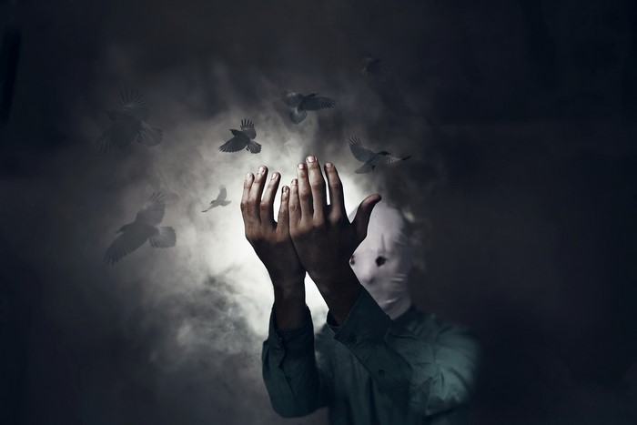 Person with masked face and hands raised with birds flying
