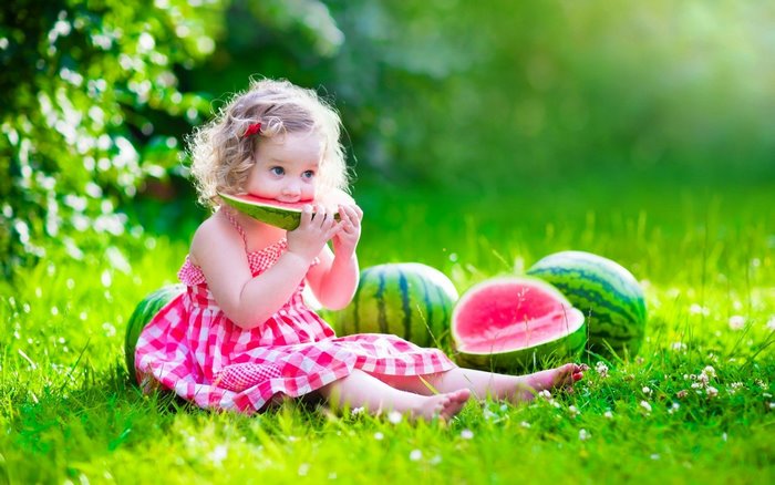 Young girl eating watermelon in a grassy field