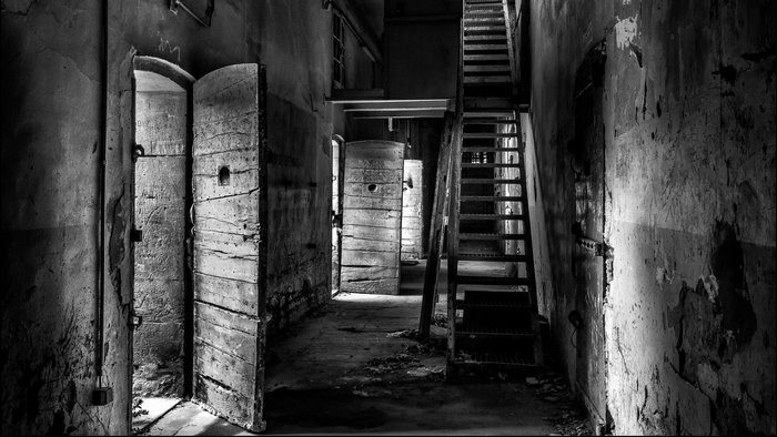 Abandoned prison hallway with cell doors and stairs