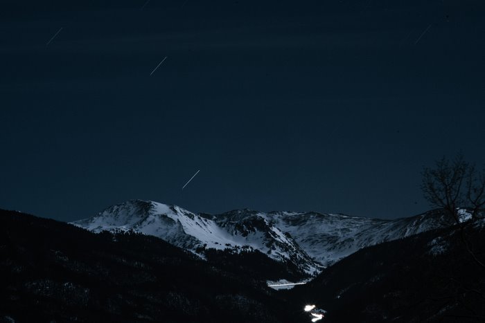 Snowy mountains under a starry night sky with light trails