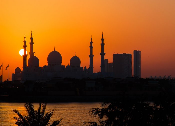 Mosque and skyscrapers silhouetted against sunset