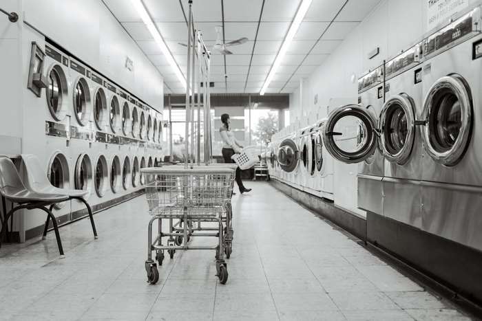Black and white image of a laundromat with a woman carrying a laundry basket