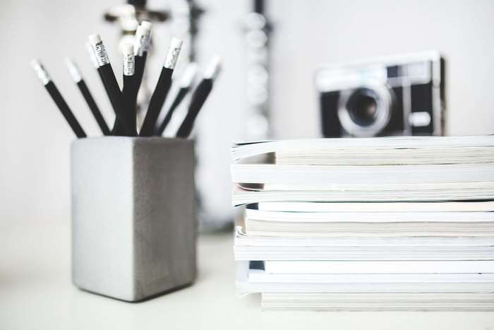 Pencils in a holder, stack of magazines, and camera on a desk