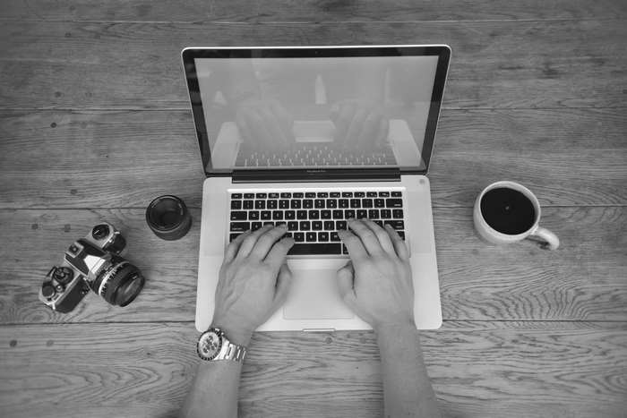 Man typing on MacBook Pro with camera and coffee