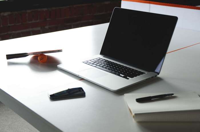 Laptop, ping pong paddle, ball, phone, and notebook on a desk