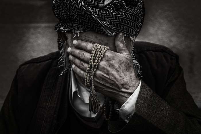 Elderly Man Covering Face with Prayer Beads