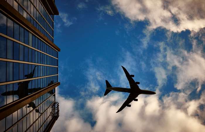 Airplane Flying Over Urban Building Against Blue Sky