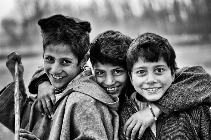 Three smiling boys in traditional clothing, black and white portrait