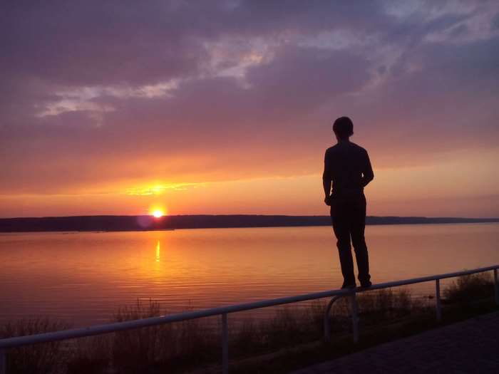 Man standing on railing watching sunset over river