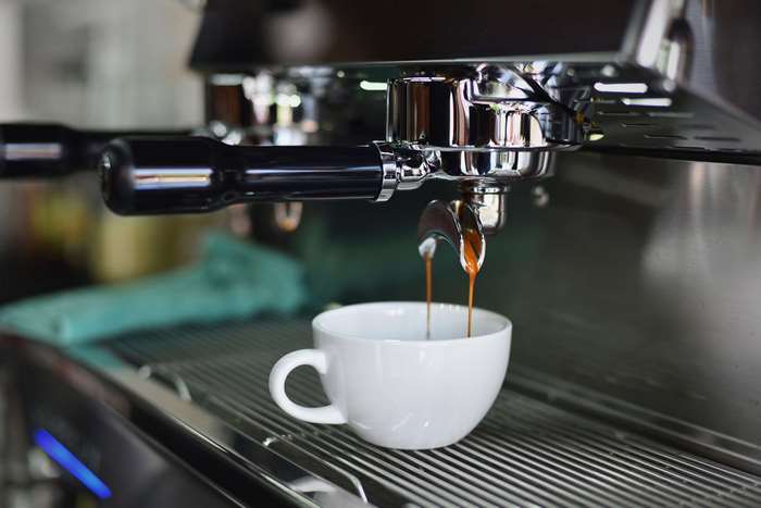 Espresso pouring from a coffee machine into a white cup