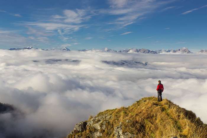 Man on mountain peak above clouds with mountain range