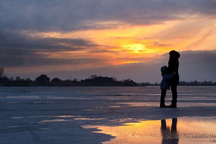 Mother and child silhouette on frozen lake at sunset